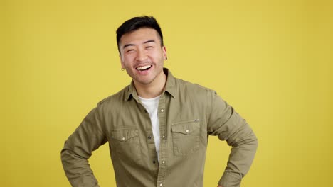 young asian man laughing and expressing joy on yellow background