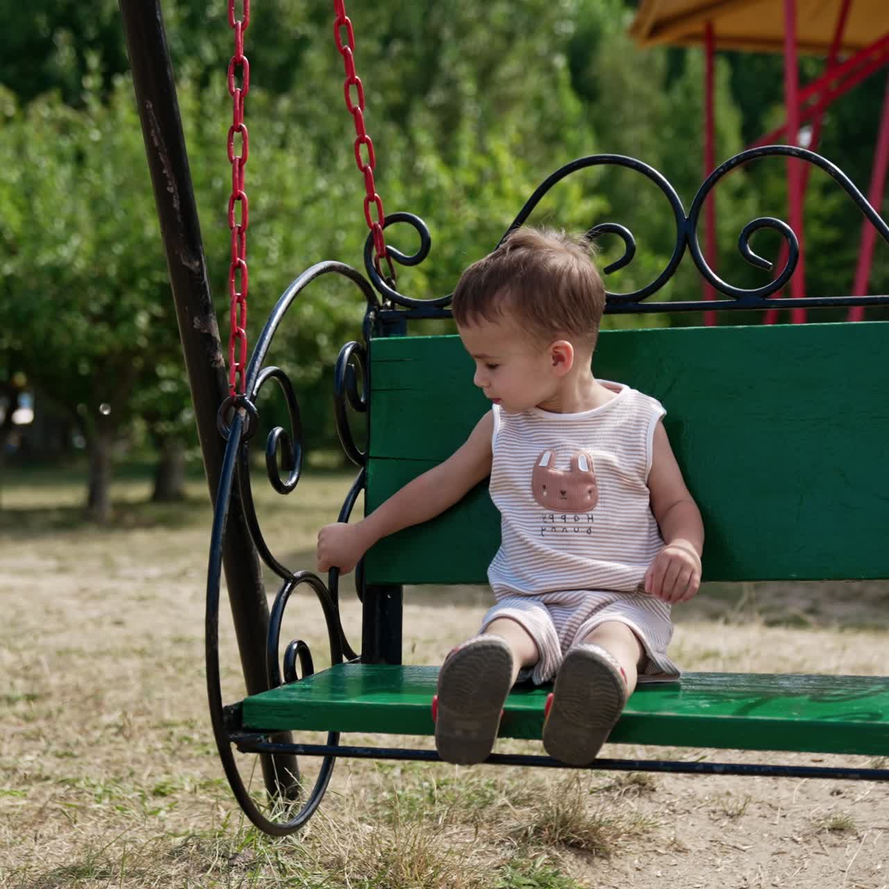 Smiling Caucasian baby boy sits on a swing. Little boy swinging in the park on sunny summer day
