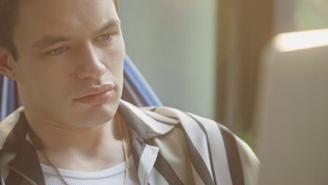 close up of a young man using laptop while sitting in a hammock