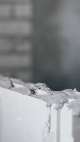 skilled painter hand in gloves holds small putty knife and puts grey substance on gypsum wall construction close view