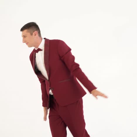 a man in a red suit with a bow-tie is parodying the flight of a bird on a white background in the studio.