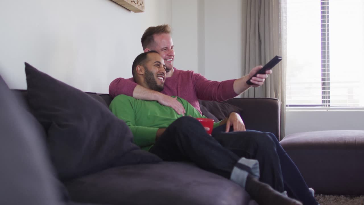 Coppia gay maschile multietnica seduta sul divano che guarda la TV