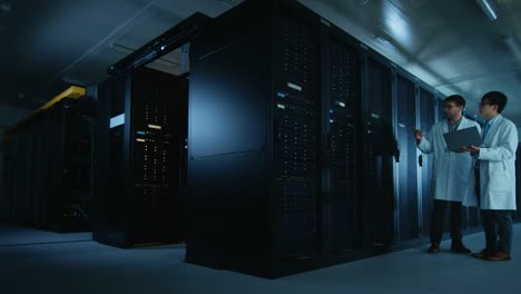 en el centro de datos: dos especialistas en informática con abrigos blancos de laboratorio, tienen una discusión sobre el trabajo de los racks de servidores. optimización del trabajo de la base de datos. computación en la nube, redes de inteligencia artificial