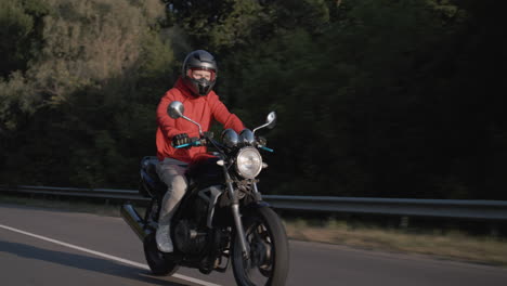 a man in a red jacket rides a motorcycle along the forest 1