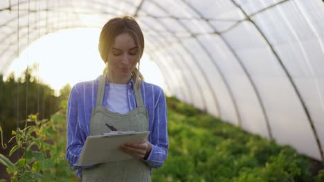 Young-woman-farmer-in-indoor-greenhouse,-accounting-plants-using-tablet