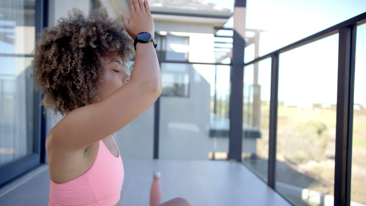 Practicing yoga, woman meditating on balcony, wearing smartwatch and sports bra