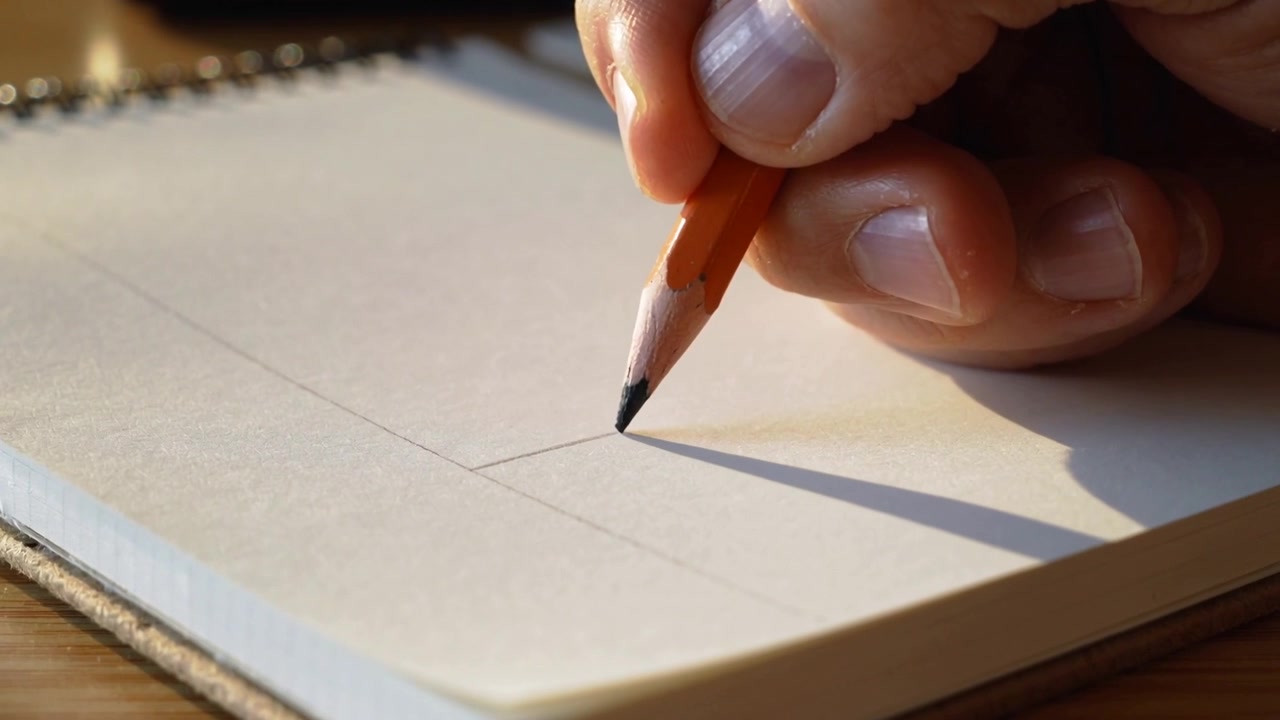 Posizionando la punta di una matita arancione su una croce guida, la mano destra che abbozza una curva su un quaderno, con spazio per il testo.