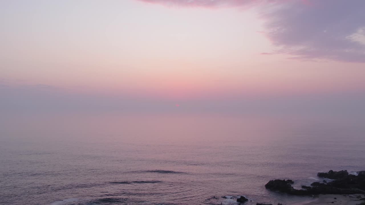 Soft pastel sunset over Praia Castro de São Paio with calm ocean and rocky shoreline