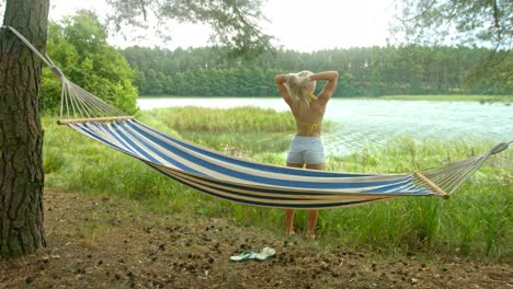 beautiful and sexy young female flips her hair looking towards the lake.  holiday surrounded by nature. standing by the hammock.