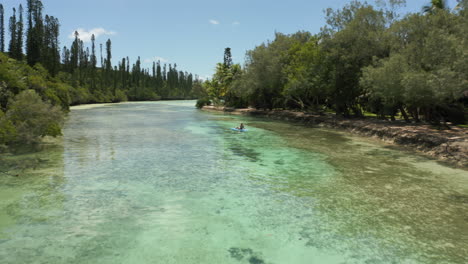 Woman-sunbathing-on-a-paddleboard-in-a-lagoon-on-the-Isle-of-Pines-New-Caledonia---aerial-flyover