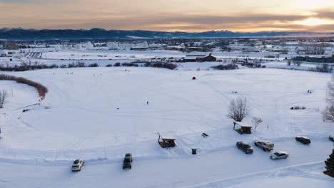 Boseman-Montana-Puesta-De-Sol-Aérea-De-Invierno-Sobre-Un-Parque-Suburbano-Nevado,-Orbita-A-La-Derecha-Con-Un-Dron-De-4k-Sobre-Pescadores-De-Hielo-Con-Fondo-De-Montaña