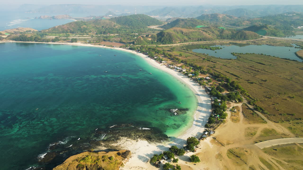 vista aérea panorámica de la playa de arena blanca de tanjung aan rodeada de agua de mar turquesa y montañas, indonesia