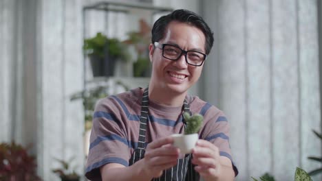 미소 짓는 아시아인 남자가 집에서 카메라에 투스 식물을 들고 보여줍니다.