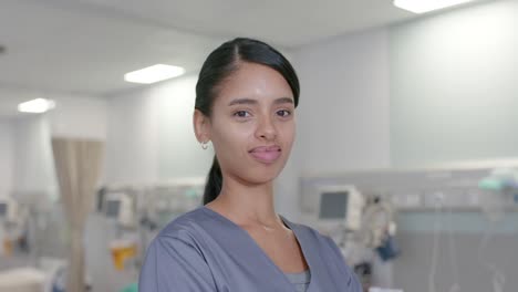 portrait of happy biracial female nurse looking at camera at hospital, in slow motion