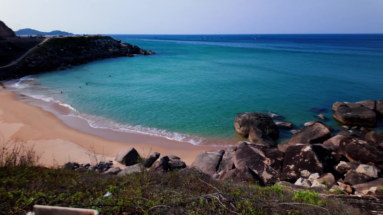 Pessoas caminham pela costa em Dak Lak, Vietnã, observando águas claras e formações rochosas. O sol brilha na areia e nas ondas. A natureza é apreciada por todos
