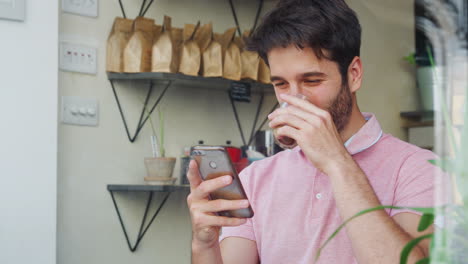 Junger-Mann-Im-Café,-Der-Auf-Sein-Mobiltelefon-Schaut