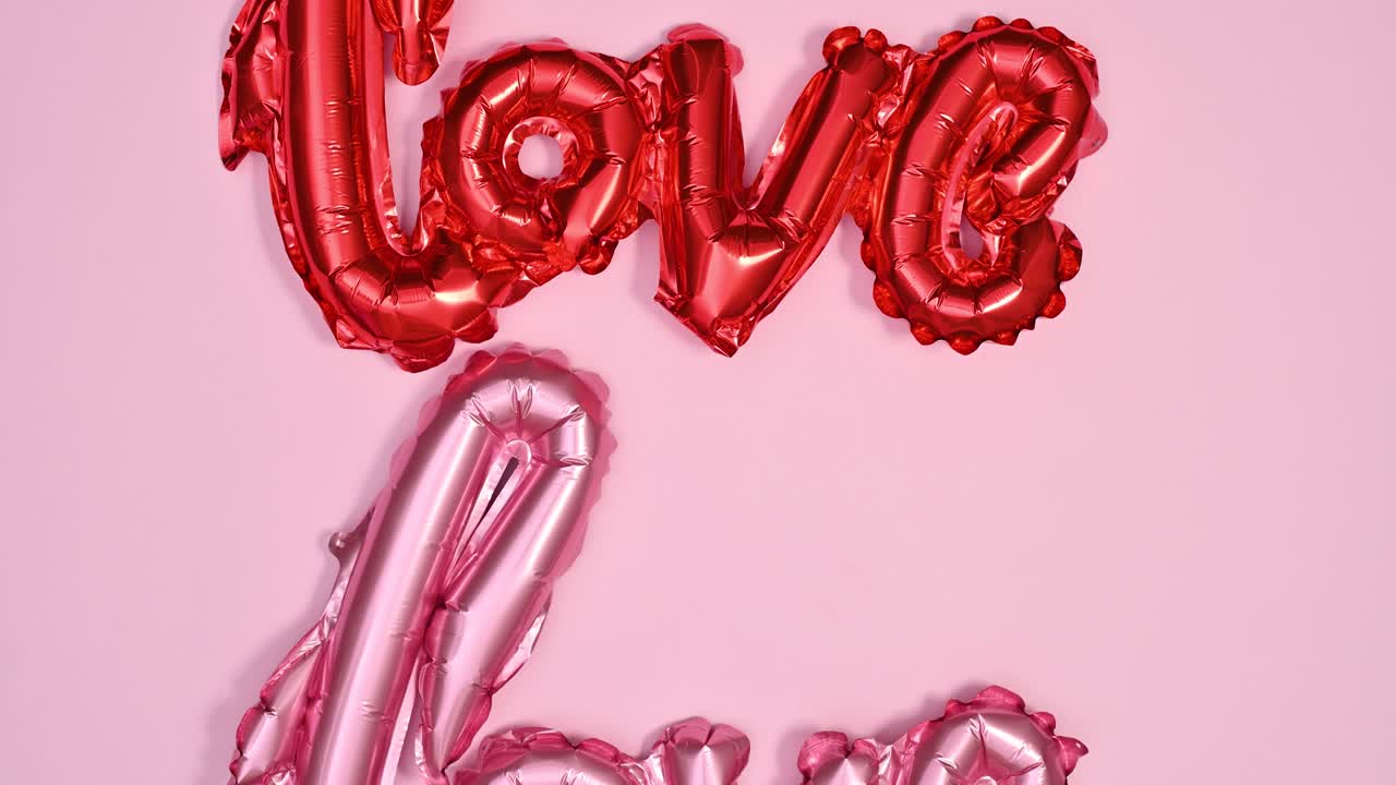 Palloncino di testo "Love" rosso e rosa che cambia su un tema rosa pastello. Composizione flat lay di San Valentino in stop motion