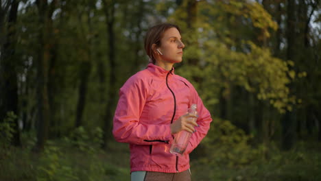 female runner resting with water bottle in forest