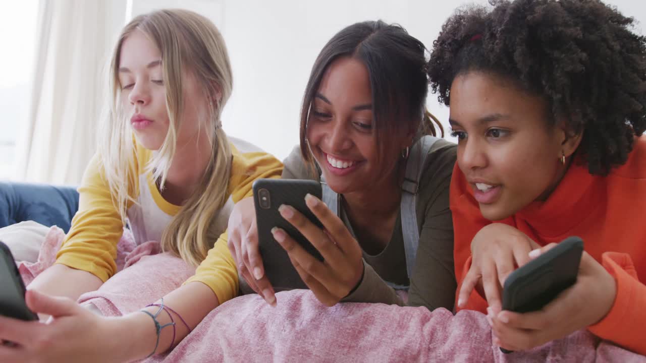 felices adolescentes diversas amigas acostadas en la cama y usando teléfonos inteligentes, cámara lenta