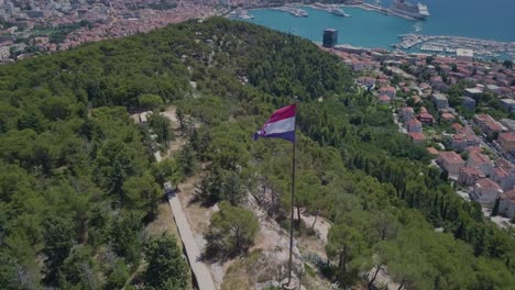 Volando-Alrededor-De-La-Bandera-De-Croacia,-Manteniéndola-Como-Tema-Principal-Y-El-Puerto-Y-La-Ciudad-De-Split-En-El-Fondo