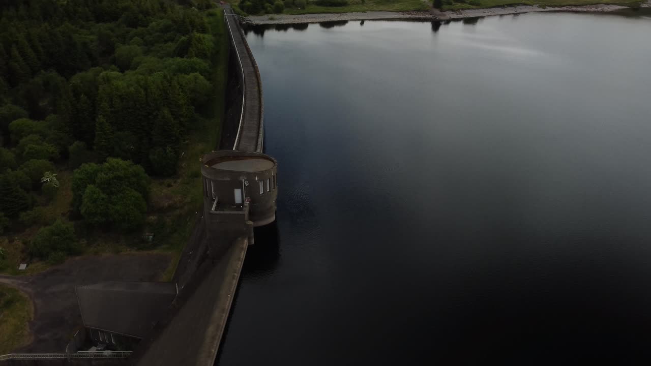 Orbital footage of a reservoir dam surrounded by trees, grass and water