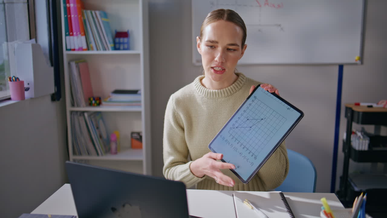 Smart tutor explaining online lesson pointing tablet screen at classroom closeup
