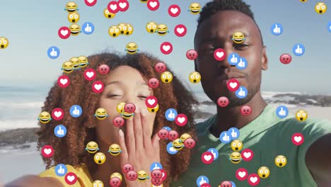 Multiple-digital-icons-floating-against-african-american-couple-blowing-kisses-looking-at-the-camera