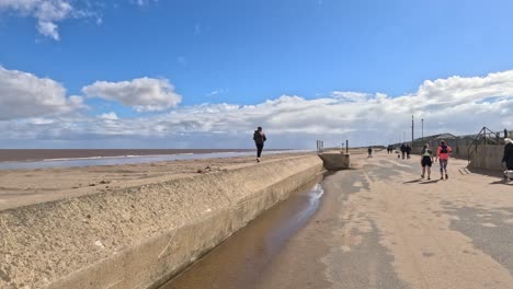 niño caminando a lo largo de una pared en el paseo marítimo por la playa en un día soleado tormentoso