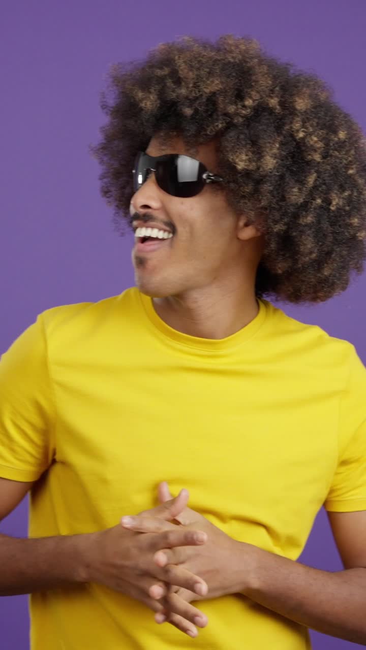 Uomo con capelli afro e occhiali da sole in posa su sfondo viola