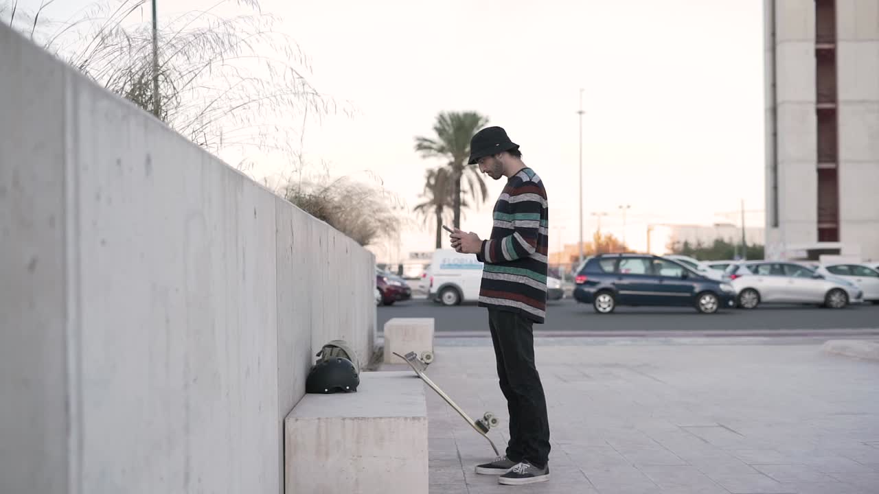 Young man using smartphone while waiting near a skateboard