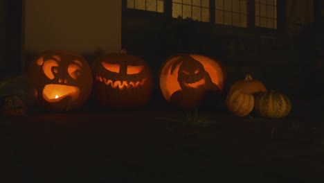 3-Geschnitzte-Beleuchtete-Kürbisse-Vor-Einem-Haus-Halloween-Mit-Rauch-Und-Kleinen-Kürbissen