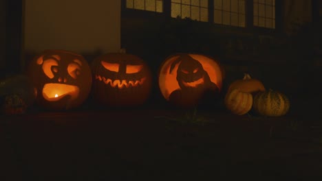 3 calabazas iluminadas talladas fuera del frente de una casa halloween con humo y calabazas pequeñas