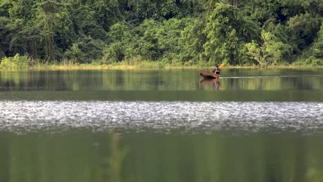 A-Man-Canoes-on-a-Reflective-Lake-with-a-Forest-Background-in-Thailand