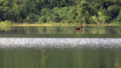un hombre navega en canoa en un lago reflectante con un fondo forestal en tailandia