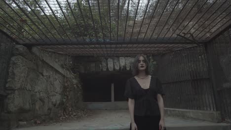 Portrait-of-Young-Female-in-Black-Dress-Standing-in-Old-Massive-Prison-Cell,-Pull-Back