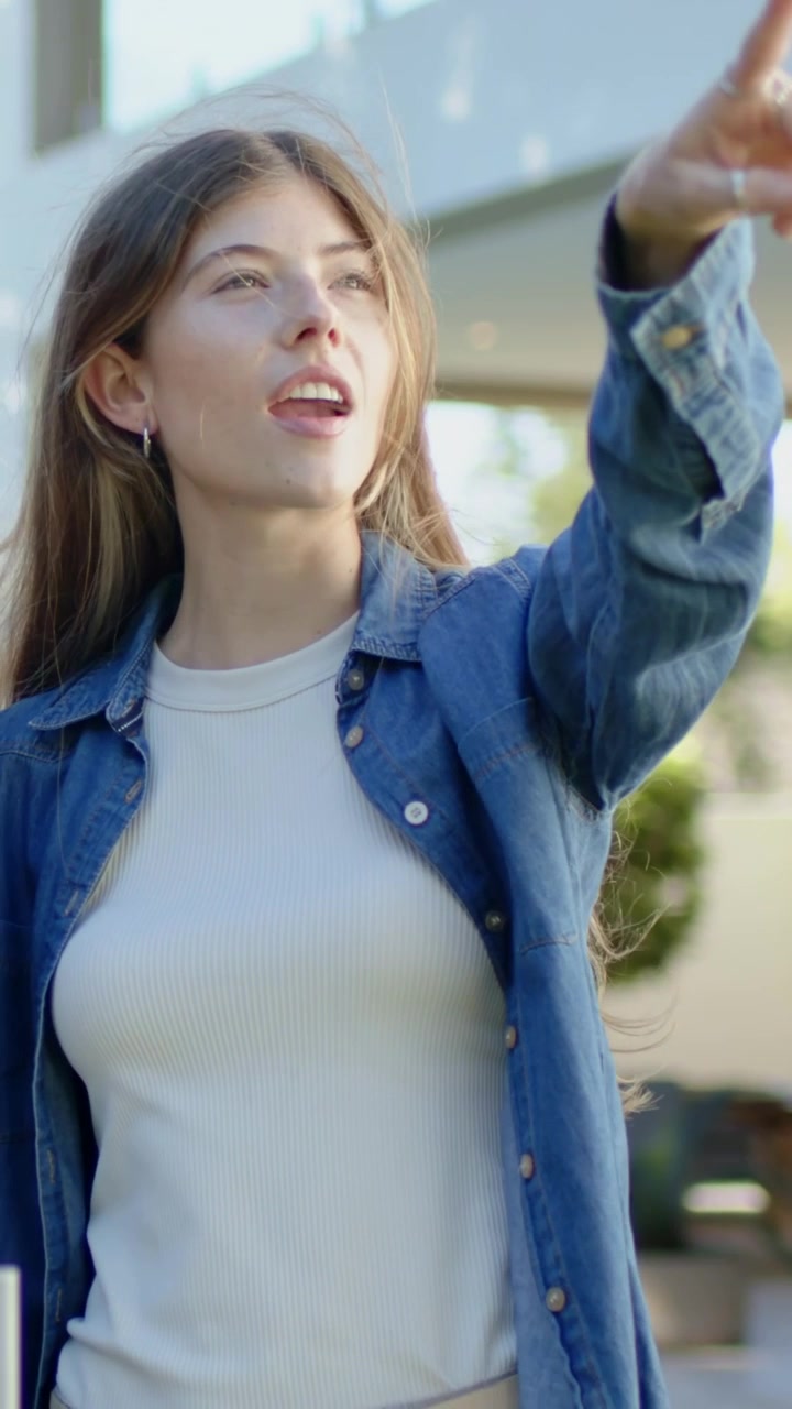 Video verticale: Donna che si alza reagendo al sole, aprendo gli occhi e allungando il braccio sul patio, con camicia di jeans.
