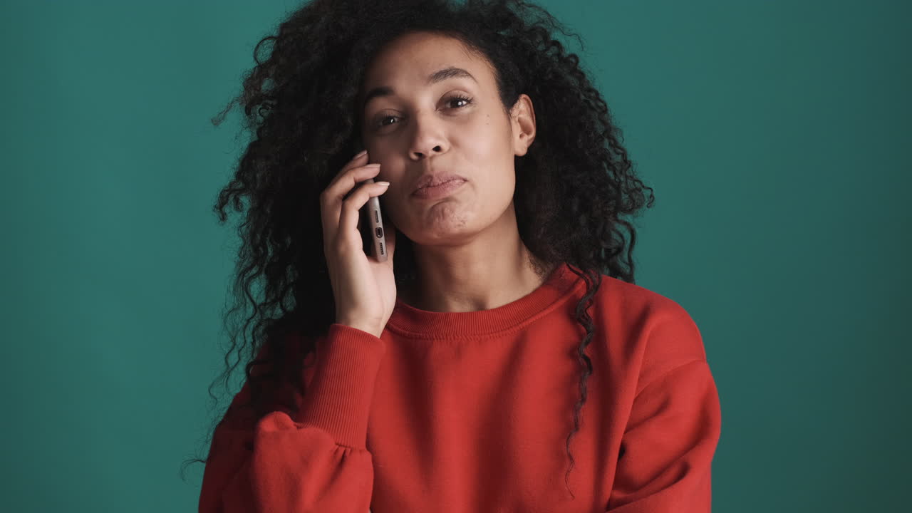 una mujer afroamericana seria usando un teléfono inteligente sobre un fondo azul.