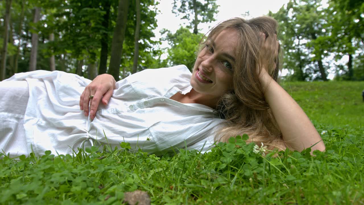 A woman laying in the soft green grass, smile and laughing while looking at the camera