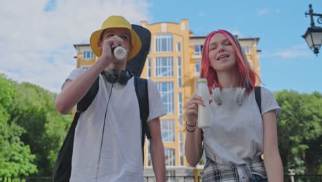 urban lifestyle of teenagers, couple of college students talking having rest drinking milk drink in bottle outdoors, city street background.