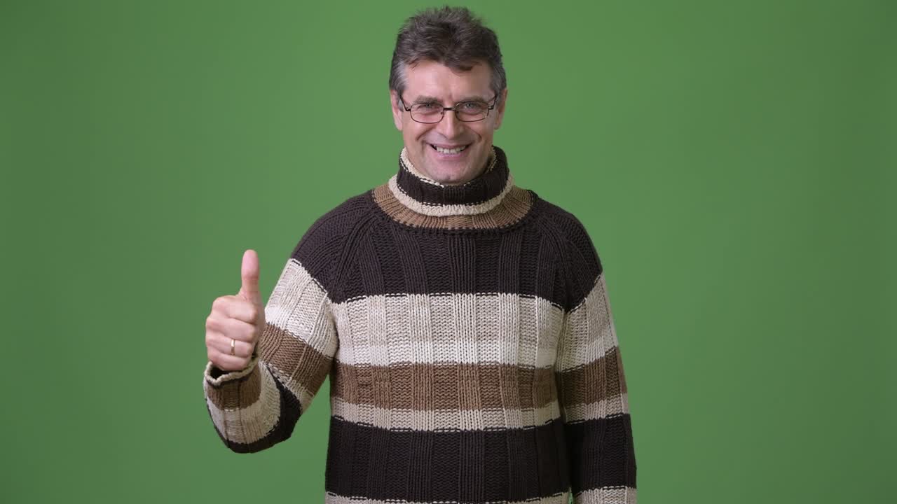 hombre guapo maduro con suéter de cuello alto contra un fondo verde