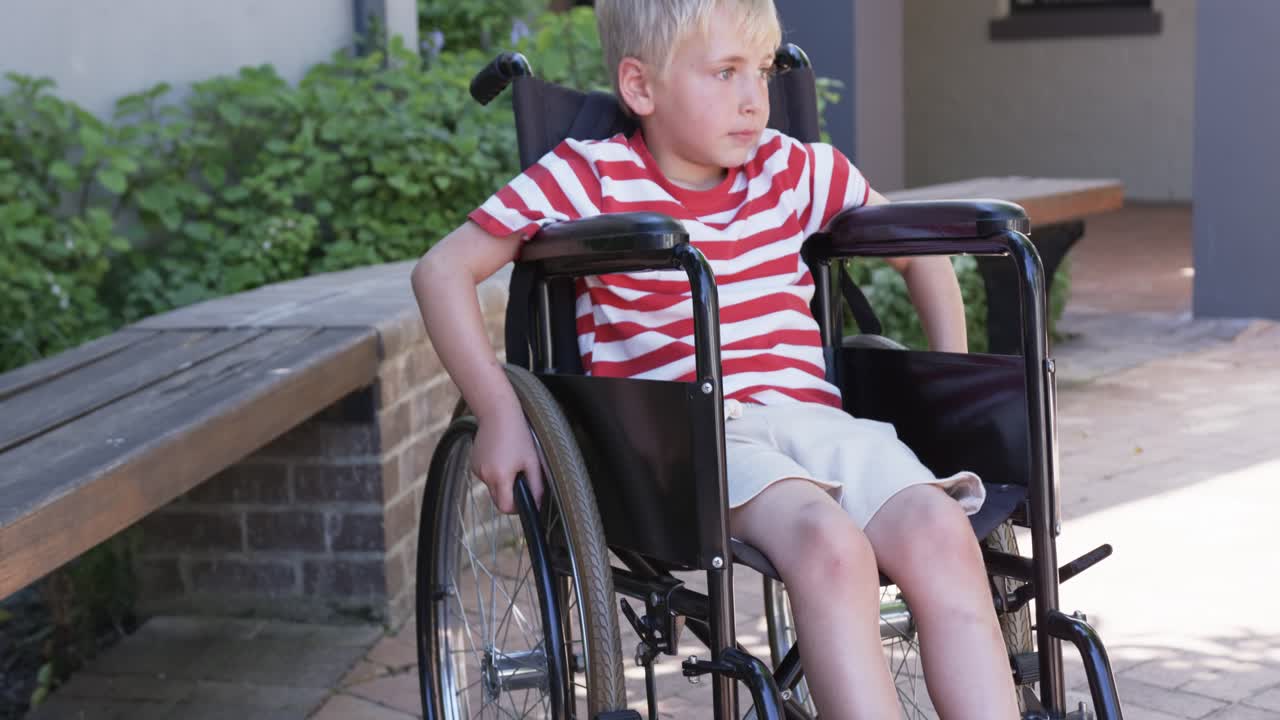 Boy in manual wheelchair in striped shirt gripping wheel while reacting to cue, turning on patio