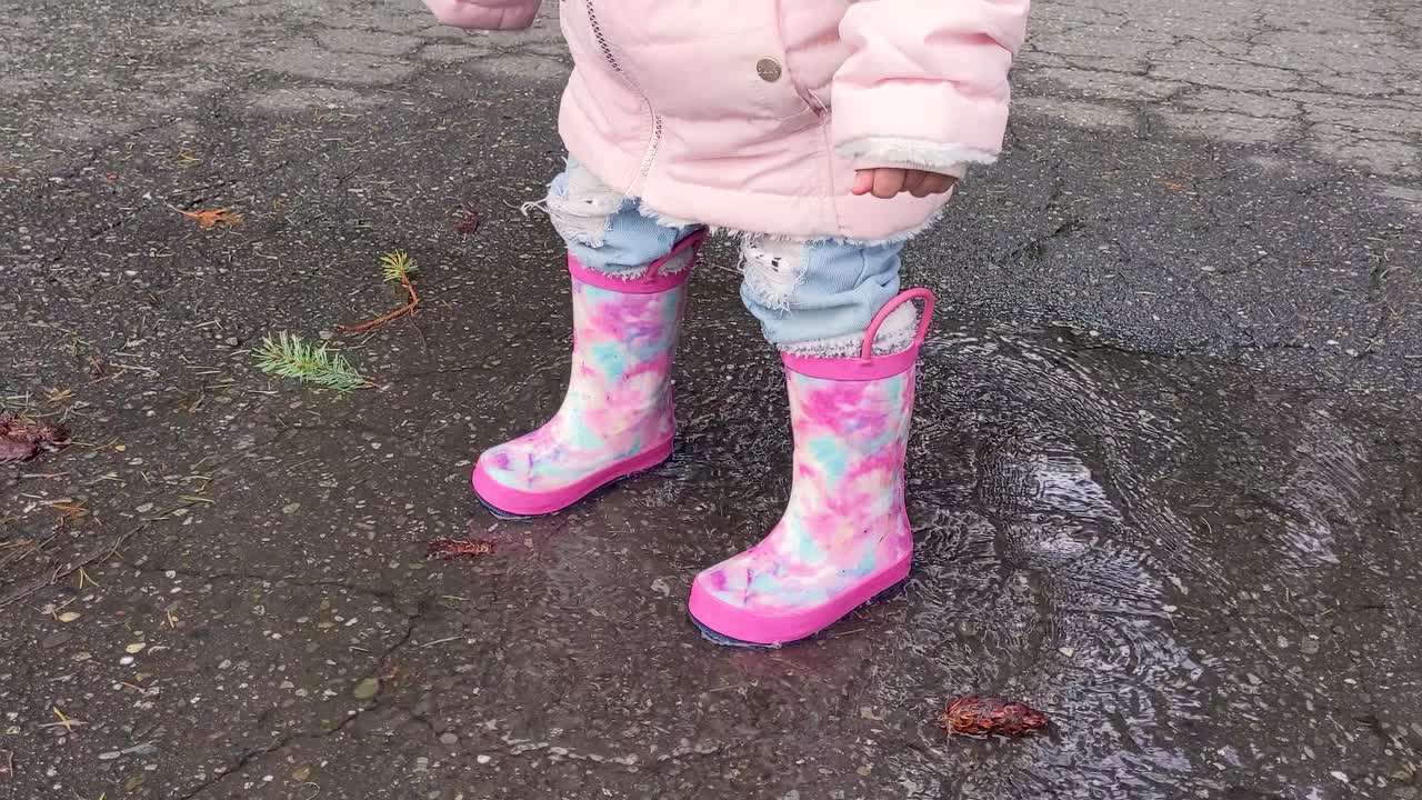Close up of a little girl wearing pink rubber boots jumping in a small puddle