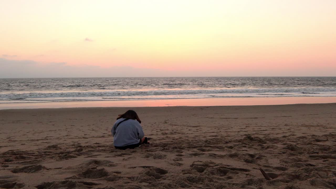Ragazza seduta da sola sulla spiaggia che guarda l'oceano e le onde dopo il tramonto.
