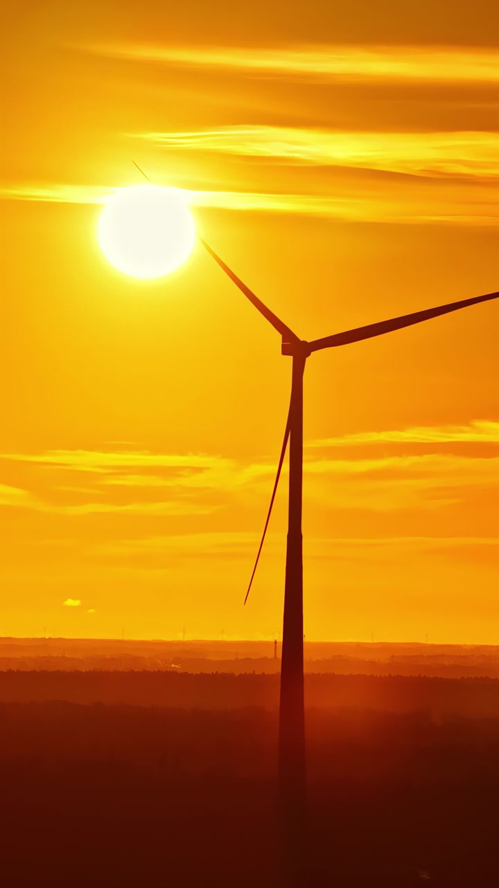 Eine Windturbine steht als Silhouette vor einem lebhaften Sonnenuntergang und bildet einen markanten Kontrast zum glühenden Himmel.