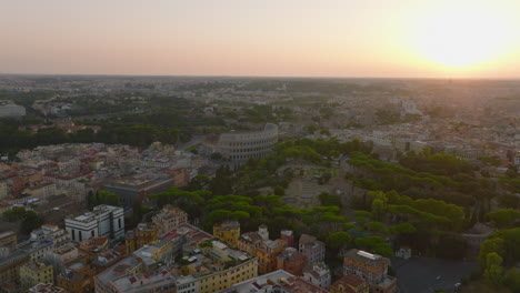 Fly-above-city-centre-at-sunset.-Oppian-Hill-park-with-historic-landmarks-and-grown-green-trees-and-ancient-Colosseum.-Rome,-Italy