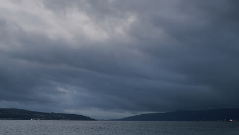 Schwere-Dunkle-Wolken-über-Küstenstadt-Und-Wasser,-Dunkles-Abendlicht