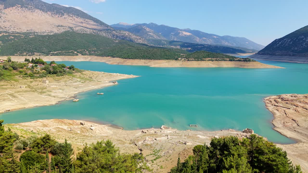 Drone establishing of turquoise water meeting dry grassy shoreline with distant mountains in Greece