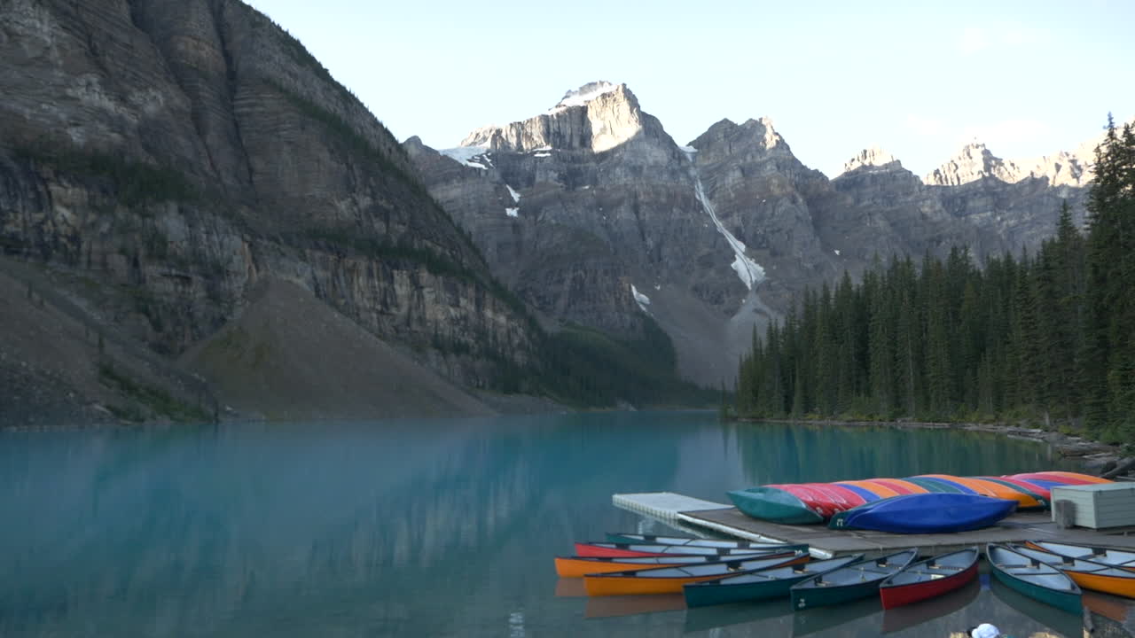 lago de morrena con coloridas canoas en el frente, y agua turquesa, montaña y árboles en la parte de atrás