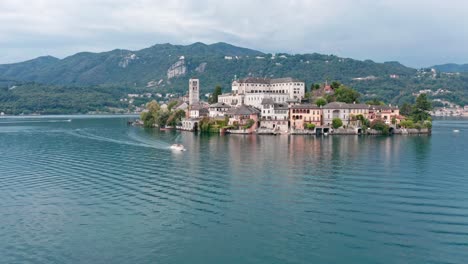 Isola-Di-San-Giulio-En-El-Lago-Orta,-Italia,-Con-Edificios-Históricos-Rodeados-De-Aguas-Tranquilas-Y-Exuberantes-Colinas-Al-Fondo,-Vista-Aérea