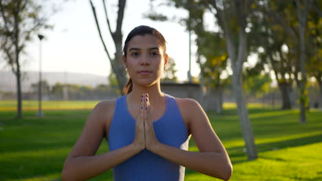 a pretty woman in a prayer hands yoga pose meditating in the park at sunrise